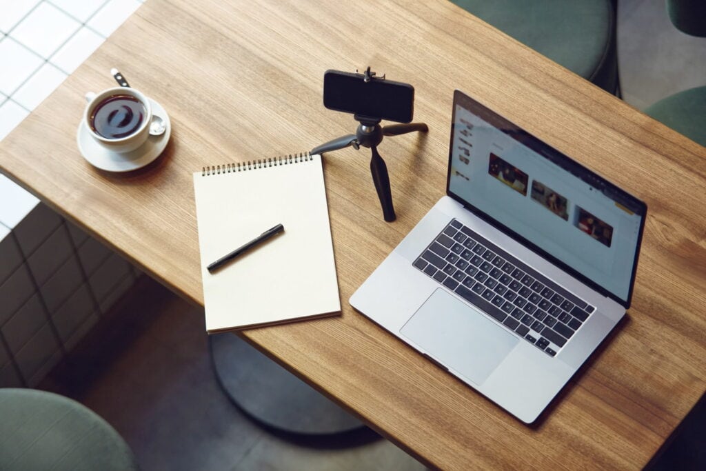 Laptop, Kamera und Notizbuch auf einem Holzschreibtisch – ideal für die Ausbildung zum freien Redner und die Selbstständigkeit im Rednergewerbe.